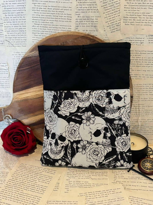 Large book sleeve featuring black and white skulls and floral design, displayed against scattered book pages background