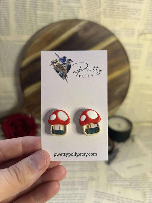 Stud earrings with polymer clay design of red and white mushroom with green and white books inside mushroom stem