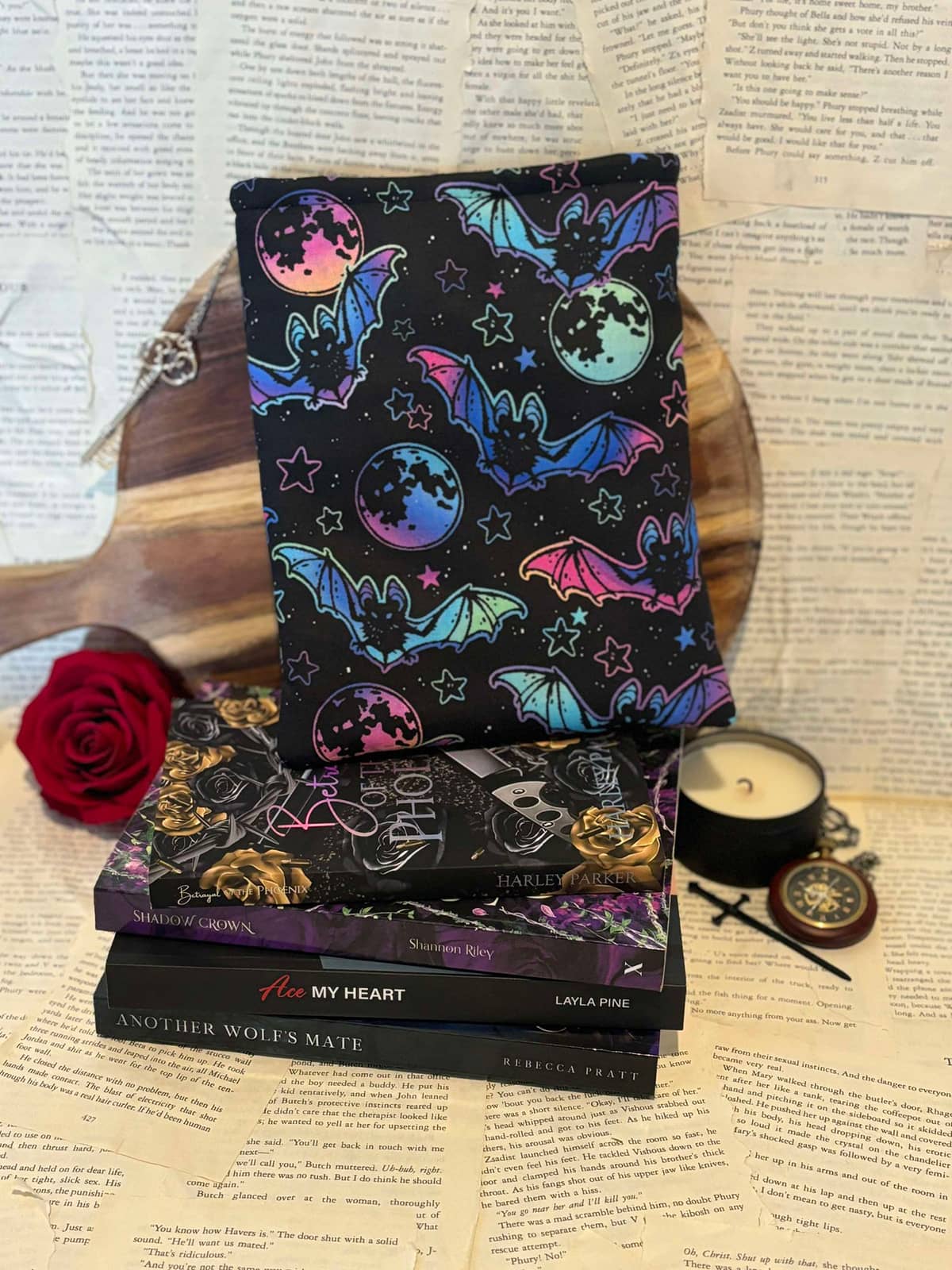 Standard book sleeve featuring neon bats and stars design on black fabric, displayed on stack of books against scattered book pages