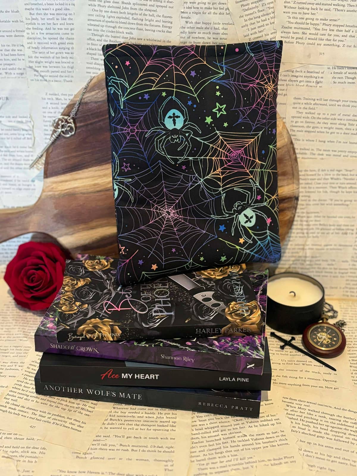 Standard book sleeve featuring neon spiders and spiderwebs design on black fabaric, displayed on stack of books against scattered book pages