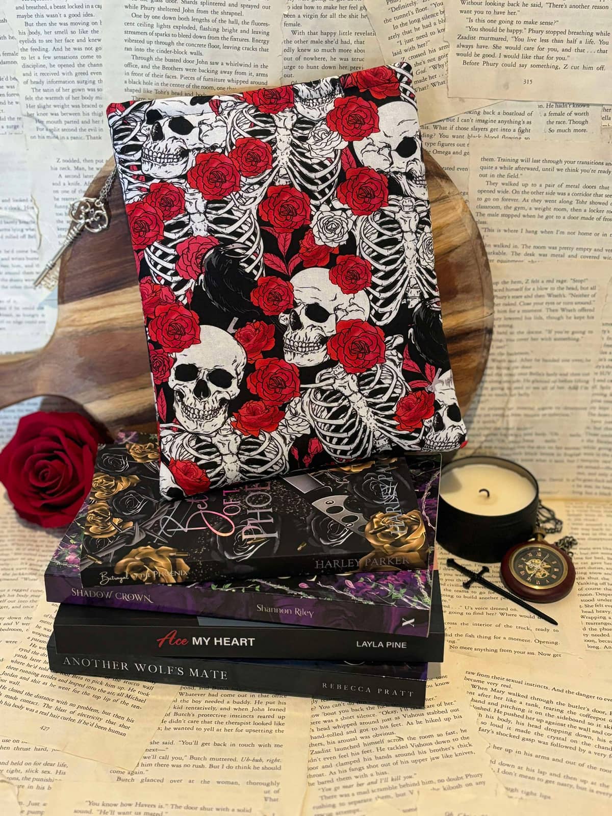 Standard book sleeve featuring red roses and white skulls design on black fabric, displayed on stack of books against scattered book pages