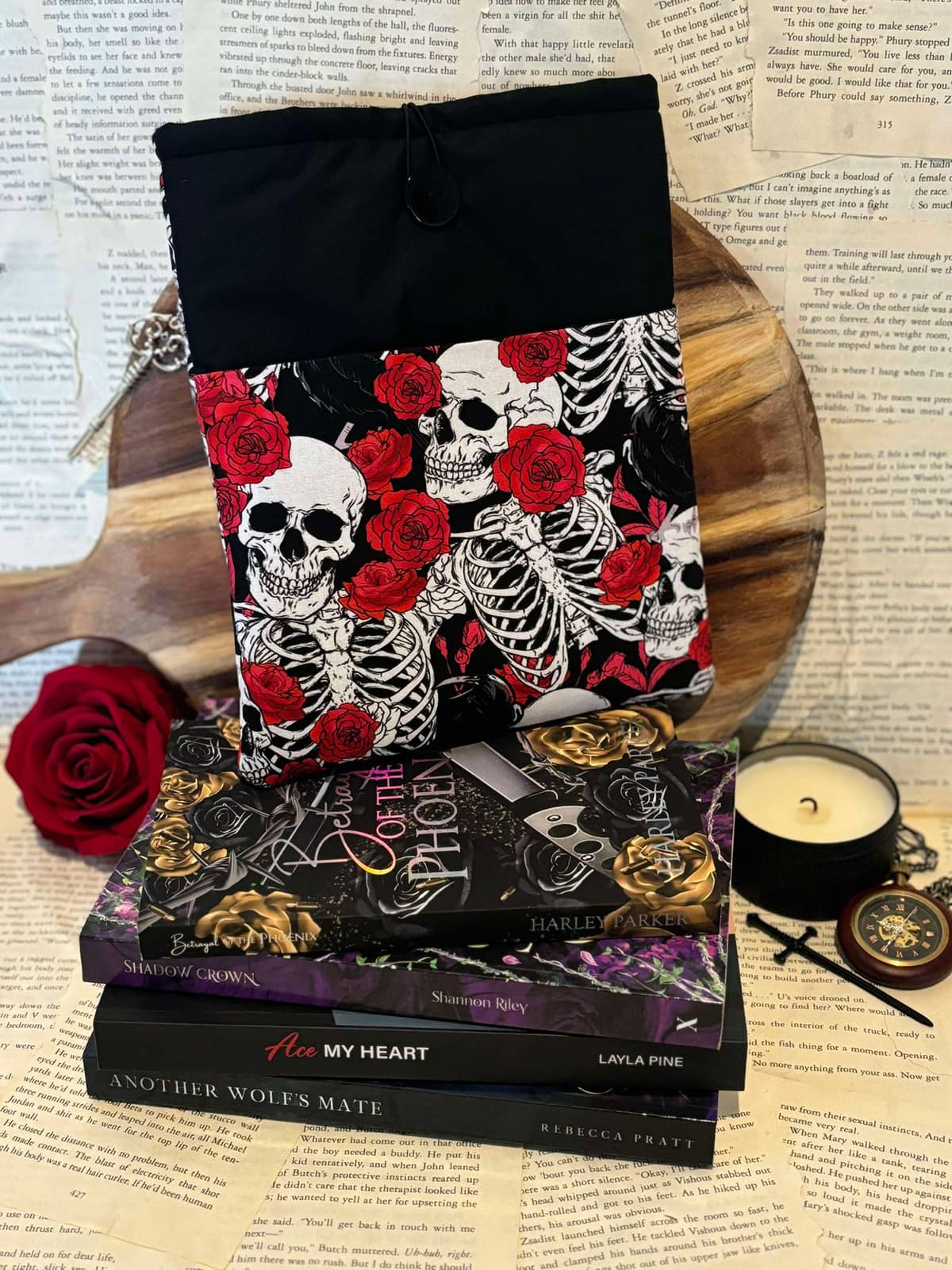 Standard book sleeve featuring red roses and white skulls design on black fabric, displayed on stack of books against scattered book pages