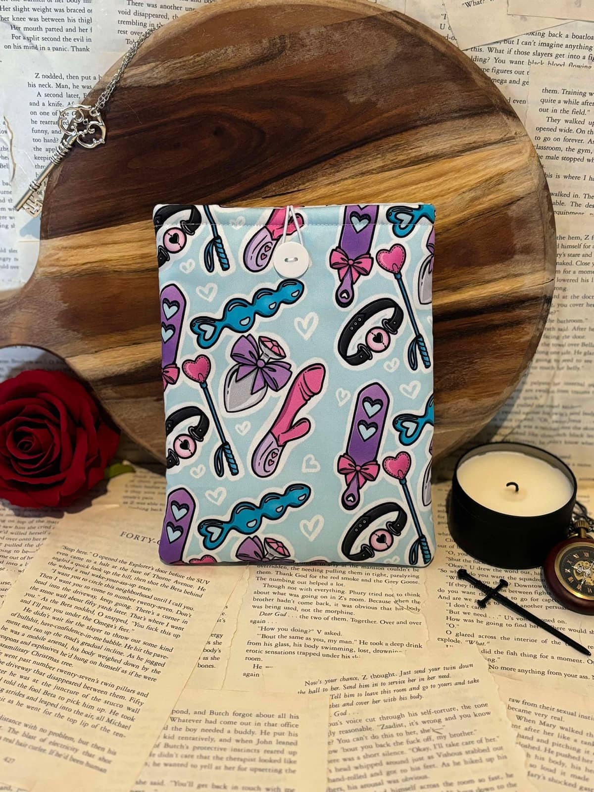 Kindle sleeve featuring light blue fabric with female adult toys design, displayed against scattered book pages