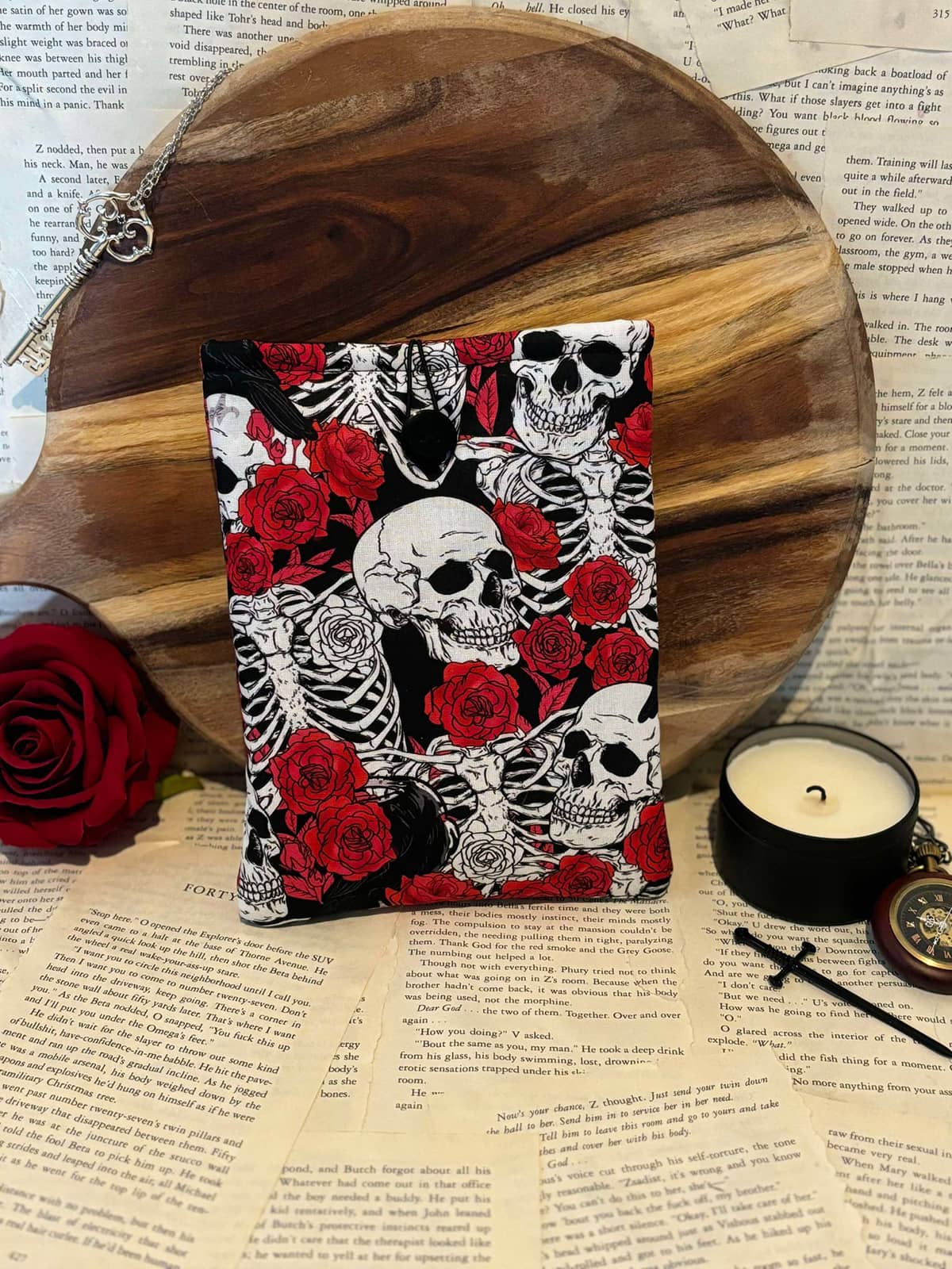 Kindle sleeve featuring red roses and white skulls design on black fabric, displayed against scattered book pages