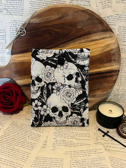 Kindle sleeve featuring white skulls and flowers design on black fabric, displayed against scattered book pages