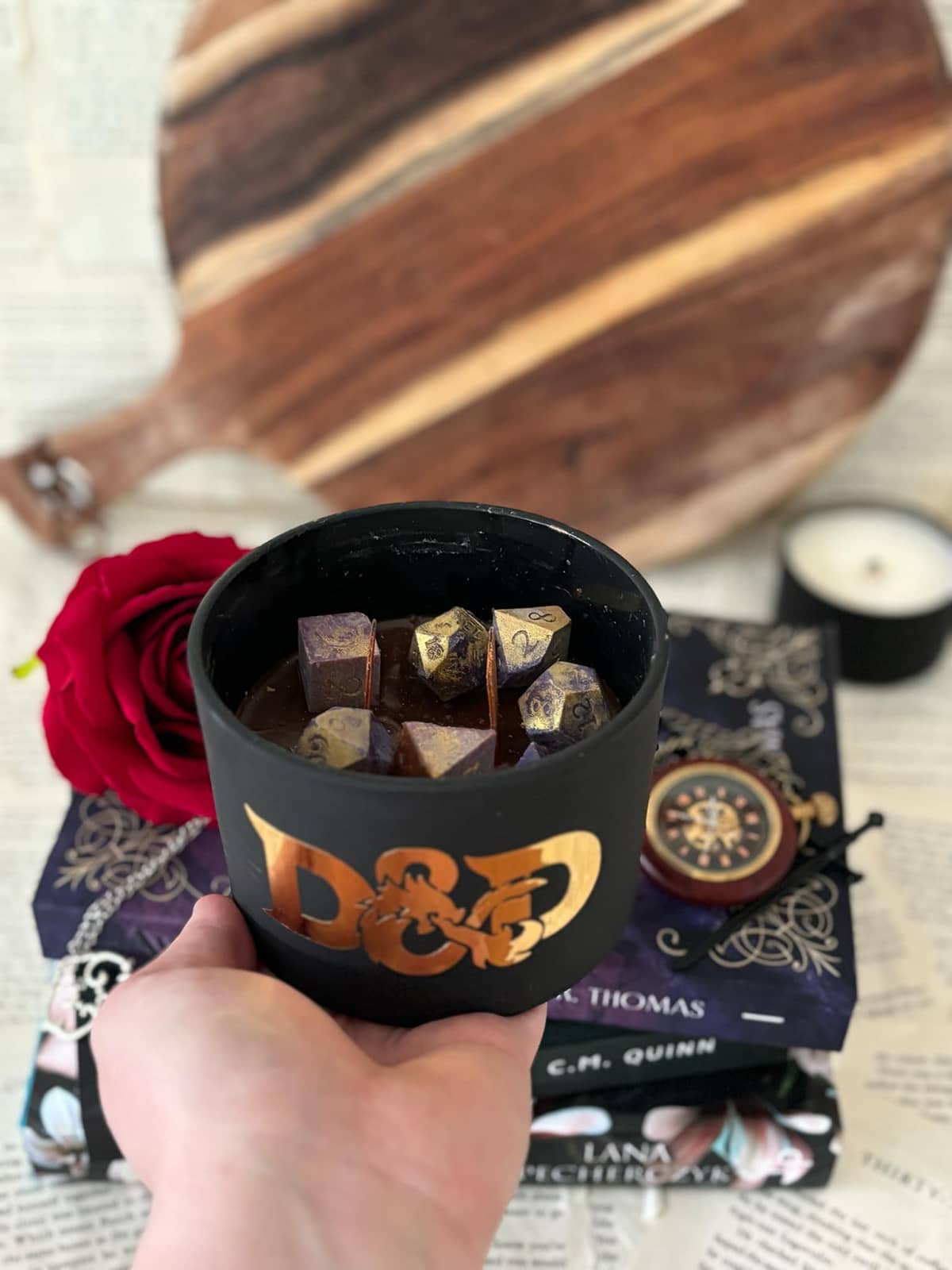 Dungeons & Dragons inspired candle, featuring themed die on top of maroon candle wax, in matte black vessel with D&D logo